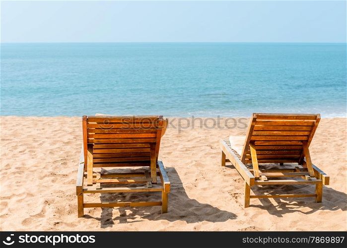 couple of empty chairs on a sandy beach in the afternoon