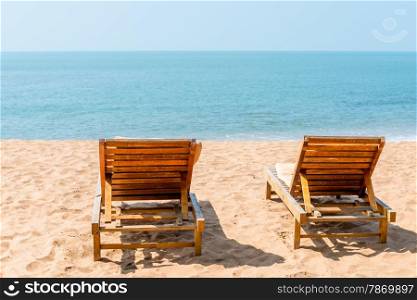 couple of empty chairs on a sandy beach in the afternoon