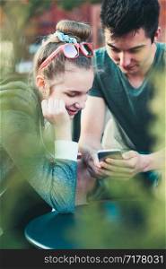 Couple of friends, teenage girl and boy, having fun with smartphones, sitting in center of town, spending time together