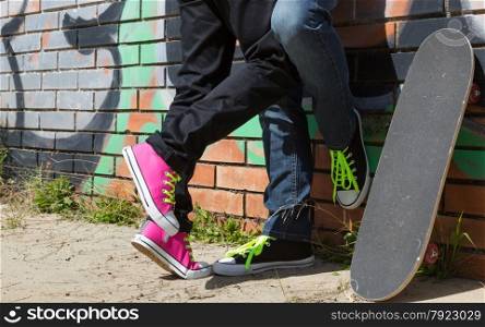 Couple of guys with his skateboard next to a wall with graffiti