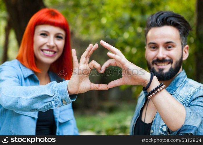 Couple of lovers forming a heart with their hands in a park