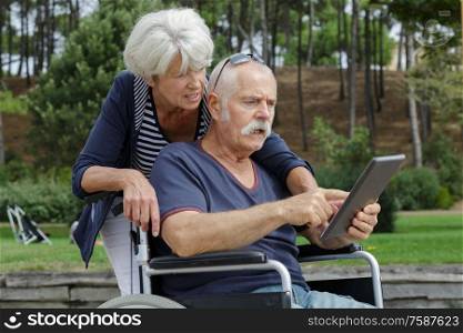 couple of retired people use a tablet in the park