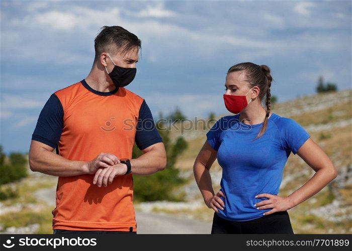 Couple of runners having a break and relaxing and preparing gear and setup time  in nature at morning wearing protective face masks
