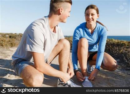 Couple of runners lace their shoes and prepare to jogging. Couple of young runners lace their shoes and prepare to jogging