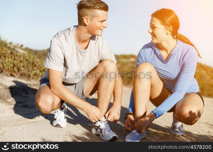 Couple of runners lace their shoes and prepare to jogging. Couple of young runners lace their shoes and prepare to jogging