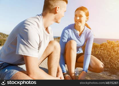 Couple of runners lace their shoes and prepare to jogging. Couple of young runners lace their shoes and prepare to jogging