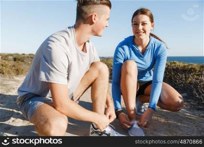 Couple of runners lace their shoes and prepare to jogging. Couple of young runners lace their shoes and prepare to jogging