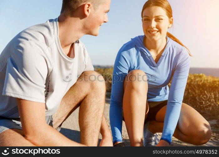 Couple of runners lace their shoes and prepare to jogging. Couple of young runners lace their shoes and prepare to jogging