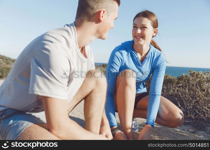 Couple of runners lace their shoes and prepare to jogging. Couple of young runners lace their shoes and prepare to jogging