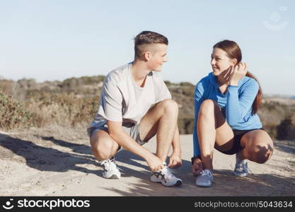 Couple of runners lace their shoes and prepare to jogging. Couple of young runners lace their shoes and prepare to jogging