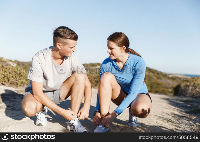 Couple of runners lace their shoes and prepare to jogging. Couple of young runners lace their shoes and prepare to jogging