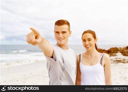 Couple of runners standing together on beach. Young couple of runners in sports wear standing together on beach and poiting at the distance