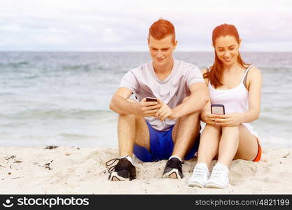 Couple of runners with mobile smart phones outdoors. Young couple of runners with mobile smart phone outdoors on beach