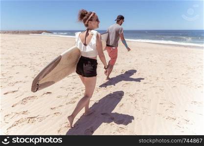 Couple of surfers with surfboards walking at a sandy beach.