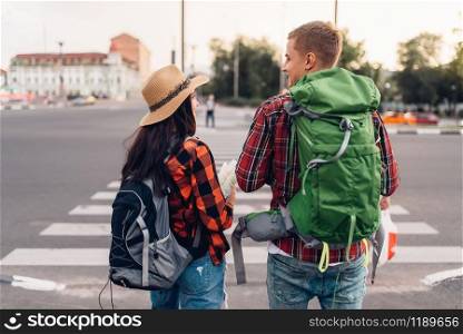 Couple of tourists with backpacks, back view, excursion in town. Summer hiking. Hike adventure of young man and woman, city walking