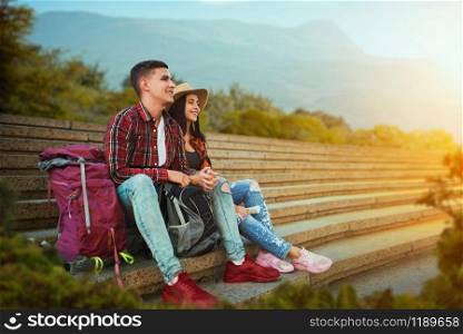 Couple of tourists with backpacks resting on the stone steps of ancient temple, excursion in town. Summer hiking. Hike adventure, travelling of young man and woman