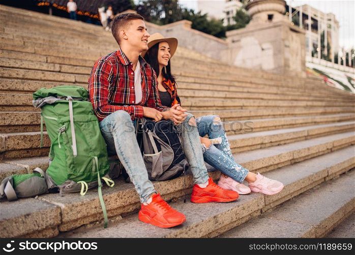 Couple of tourists with backpacks resting on the stone steps of ancient temple, excursion in town. Summer hiking. Hike adventure, travelling of young man and woman. Tourists resting on the steps of ancient temple