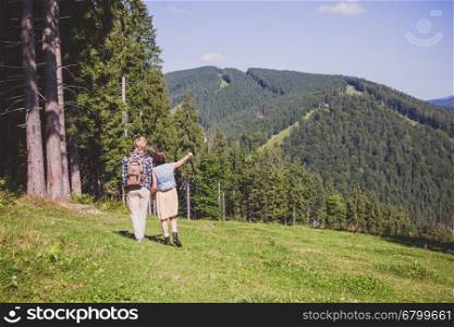 Couple of travelers walking at the summer meadow and looking around mountain view