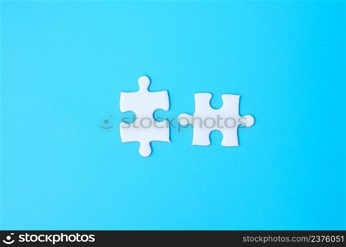 couple of white puzzle jigsaw pieces on blue background. Concept of solutions, mission, success, goals, cooperation, partnership, strategy and puzzle day