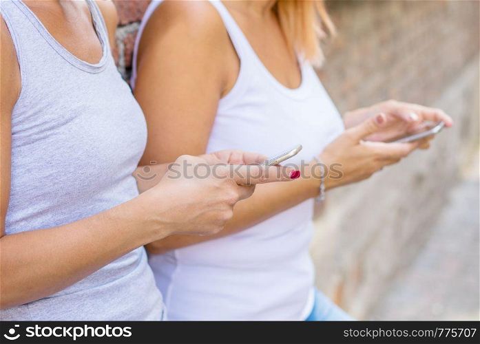 couple of woman watching smart mobile phones near a brick wall