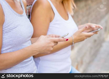 couple of woman watching smart mobile phones near a brick wall