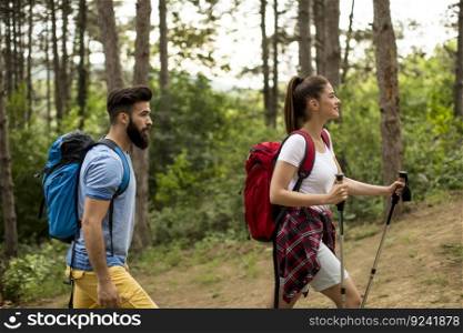 Couple of young happy travelers hiking with backpacks on the beautiful forest trail on a summer day