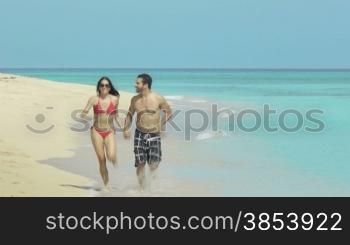 Couple of young newlyweds walking hand in hand on the beach in Cuba