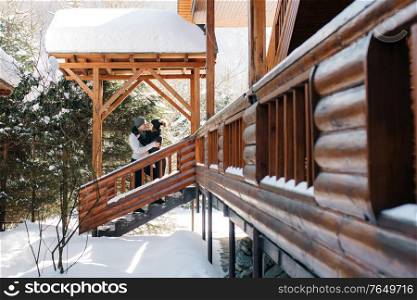 couple of young people a guy and a girl on the porch of a snow-covered wooden house in the winter mountains