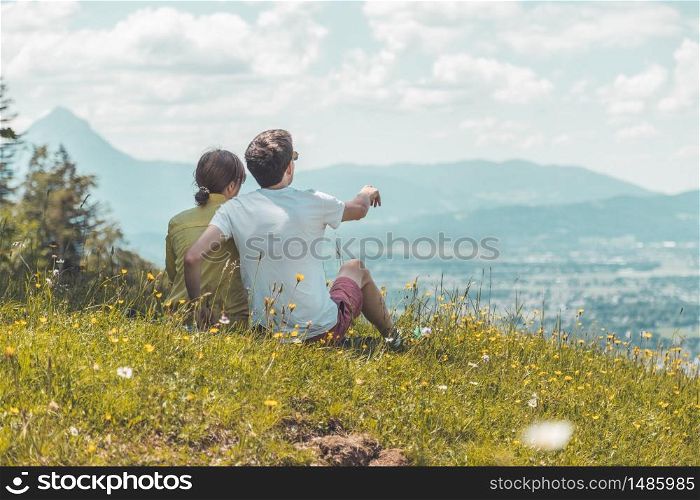 Couple on a hiking trip is sitting on the meadow an enjoying the view over the far away city