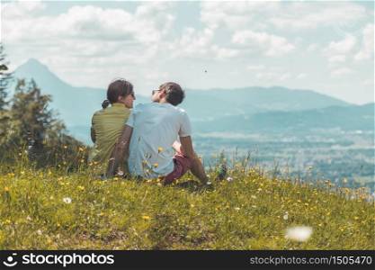 Couple on a hiking trip is sitting on the meadow an enjoying the view over the far away city