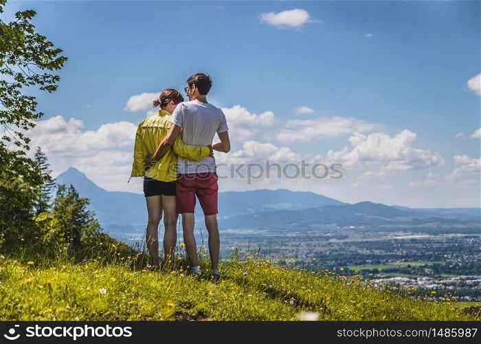 Couple on a hiking trip is standing on the meadow an enjoying the view over the far away city