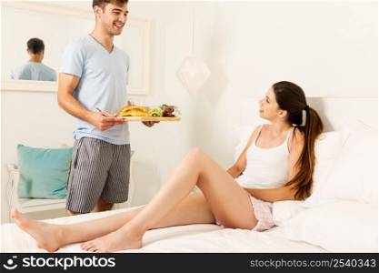 Couple on a hotel room, and the man serving breakfast on bed