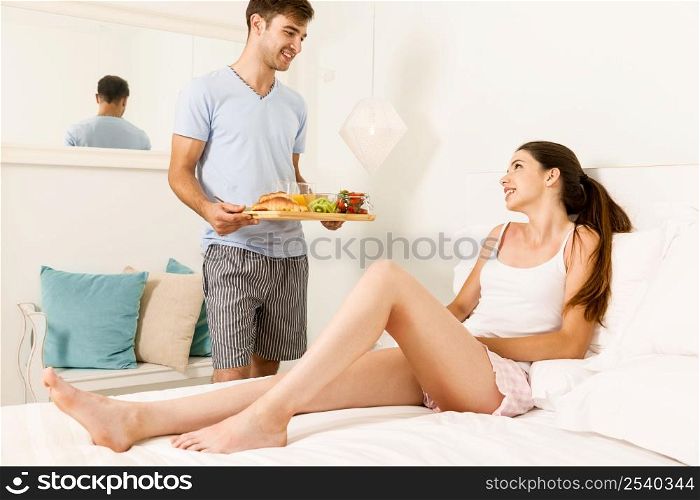 Couple on a hotel room, and the man serving breakfast on bed