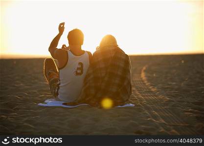 Couple on beach, at sunset, young woman wrapped in blanket, rear view