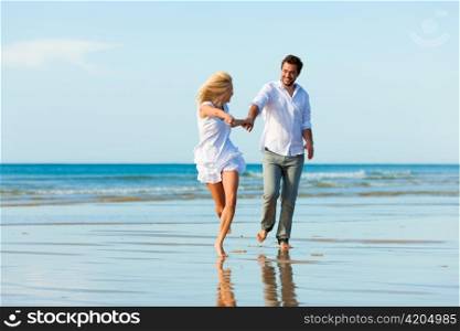 Couple on the beach in white clothing running down, they might be on vacation or even honeymoon