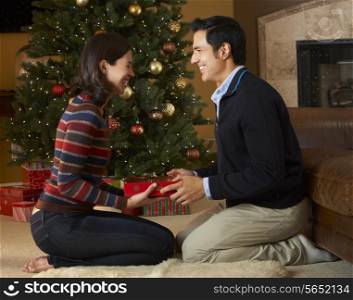 Couple Opening Presents In Front Of Christmas Tree