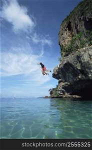 Couple outdoors jumping off cliff into ocean