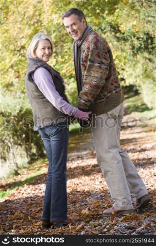 Couple outdoors on path in park holding hands and smiling (selective focus)