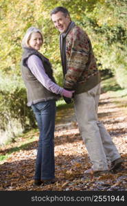 Couple outdoors on path in park holding hands and smiling (selective focus)