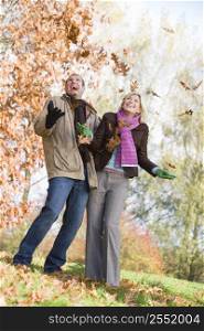 Couple outdoors playing in leaves and smiling (selective focus)