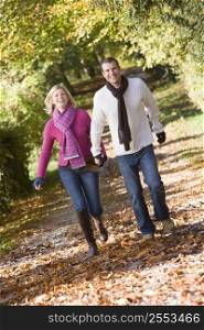 Couple outdoors running on path in park holding hands smiling (selective focus)