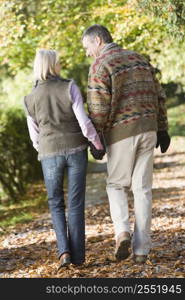 Couple outdoors walking on path in park holding hands and smiling (selective focus)
