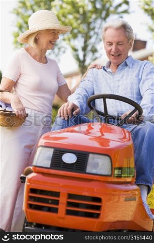 Couple outdoors with tools and lawnmower smiling