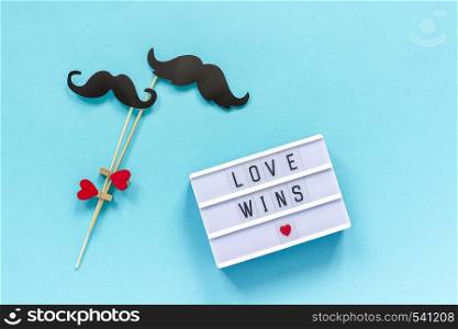 Couple paper mustache props and Light box with text Love wins on blue background. Concept Homosexuality gay love National Day Against Homophobia or International Gay Day Top view Greeting card. Couple paper mustache props and light box with text Love wins on blue background. Concept Homosexuality gay love. National Day Against Homophobia or International Gay Day Top view Greeting card