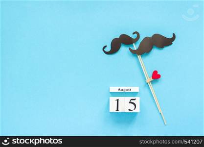 Couple paper mustache props fastened clothespin heart and calendar 15 August on blue background. Concept Homosexuality gay love. International Gay Day Top view pace Template for text or design.. Couple paper mustache props fastened clothespin heart and calendar 15 August on blue background. Concept Homosexuality gay love. International Gay Day Top view pace Template for text or design