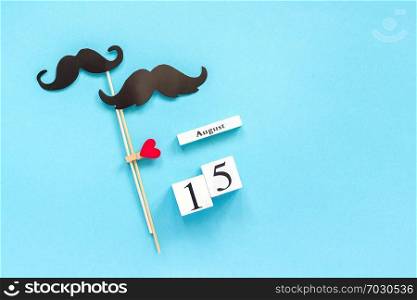 Couple paper mustache props fastened clothespin heart and calendar 15 August on blue background. Concept Homosexuality gay love. International Gay Day Top view pace Template for text or design.. Couple paper mustache props fastened clothespin heart and calendar 15 August on blue background. Concept Homosexuality gay love. International Gay Day Top view pace Template for text or design