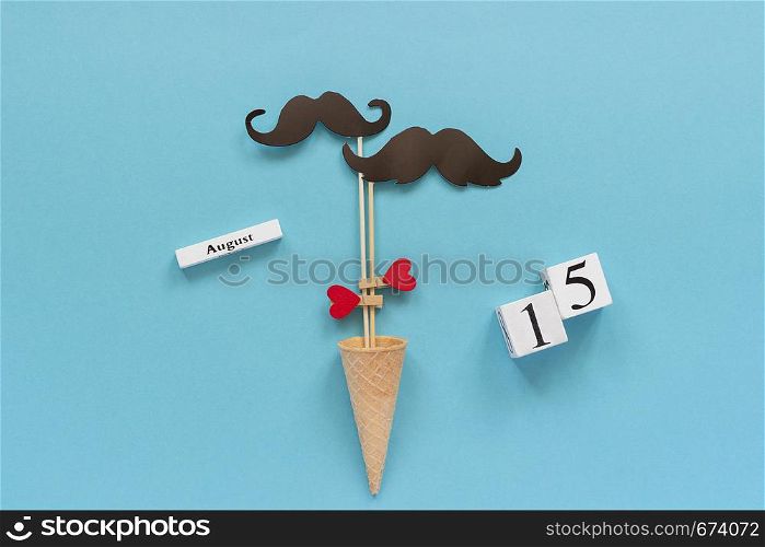 Couple paper mustache props fastened heart in ice cream cone and calendar 15 August on blue background. Concept Homosexuality gay love, International Gay Day.. Couple paper mustache props fastened heart in ice cream cone and calendar 15 August on blue background. Concept Homosexuality gay love, International Gay Day