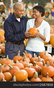 Couple picking out pumpkins and smiling at outdoor market.