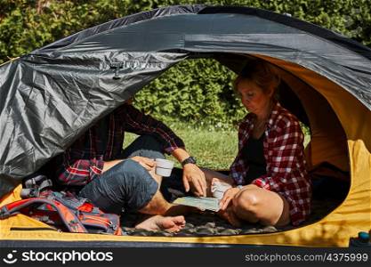 Couple planning next trip while sitting with map in tent. People relaxing in tent at camping during summer vacation. Actively spending vacations outdoors close to nature. Concept of camp life