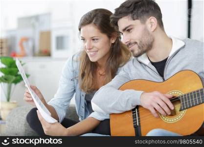 couple playing acoustic guitar together sitting on sofa